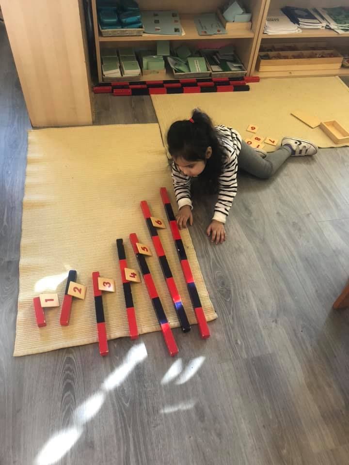 A child working alone on the floor with the Montessori number rods